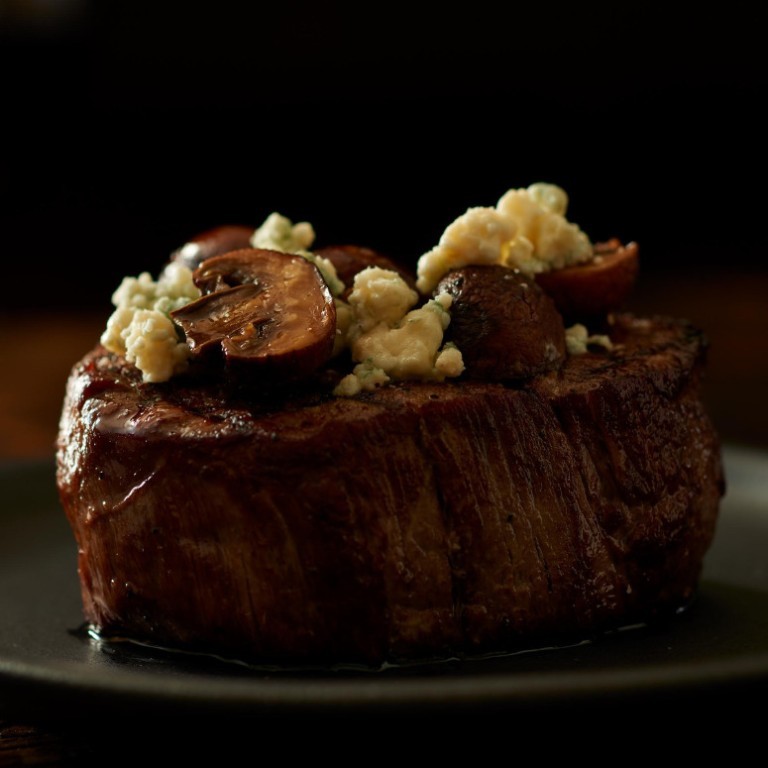 A centre-cut filet under mushrooms and blue cheese, lit low against a dark ground.