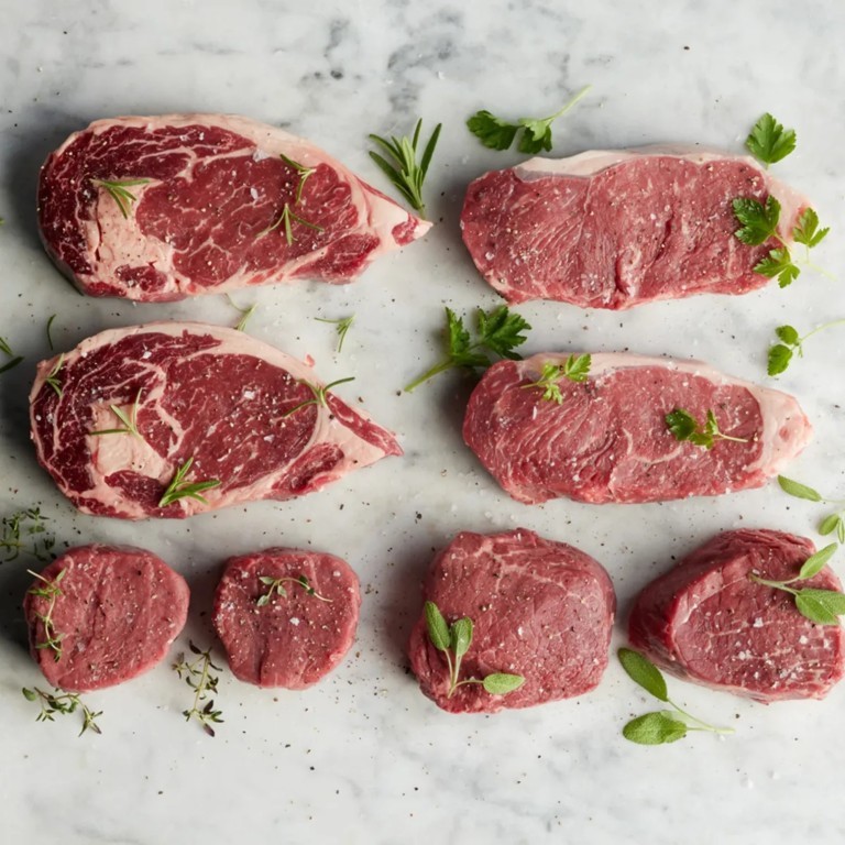 Ribeyes, strips and filets laid out raw on a marble slab.