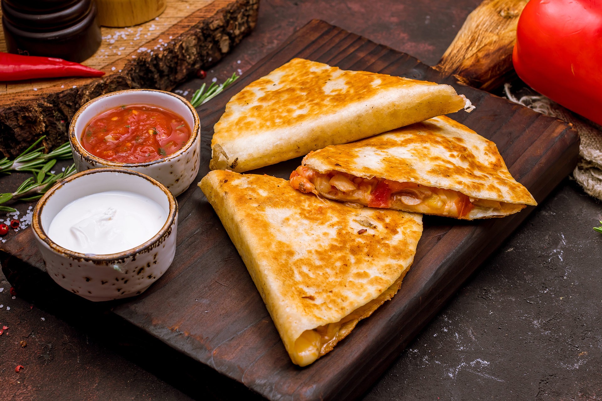 Quesadilla wedges fanned across a wooden board with small bowls of salsa and sour cream.