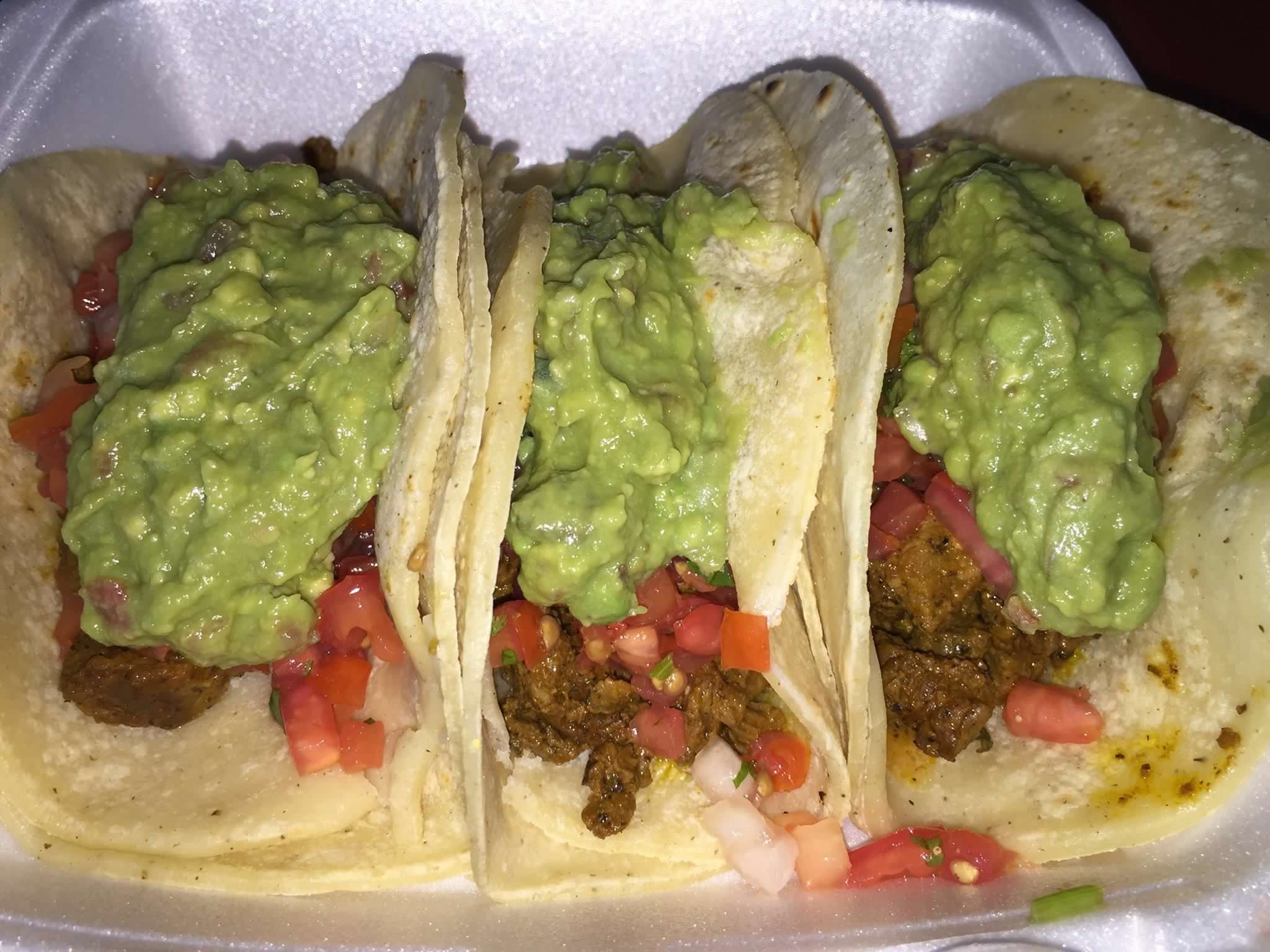 Three soft tacos loaded with meat, guacamole and pico de gallo, side by side on a tray.