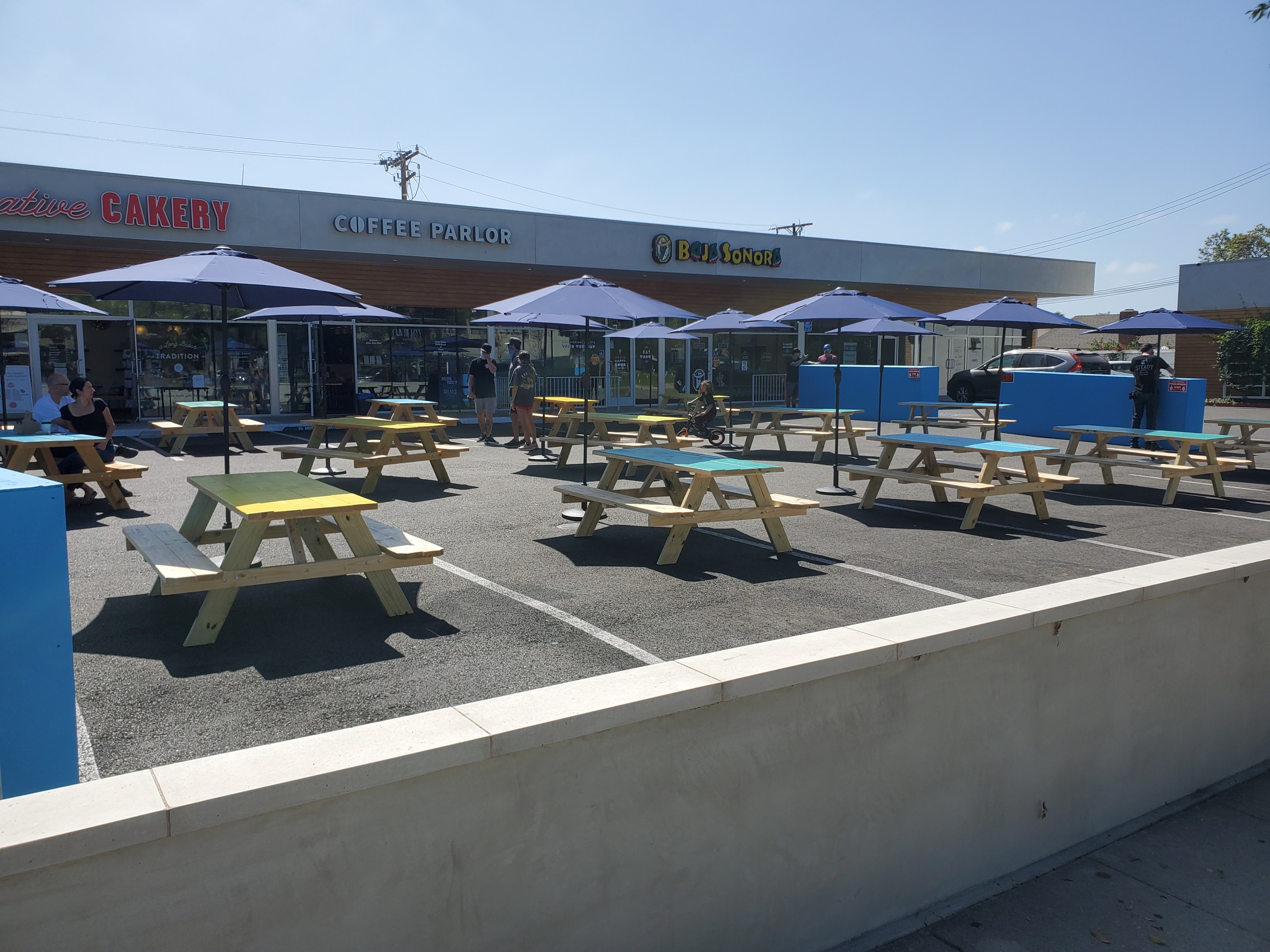 Picnic tables with brightly painted tops, shaded by blue umbrellas, on the patio outside the restaurant.