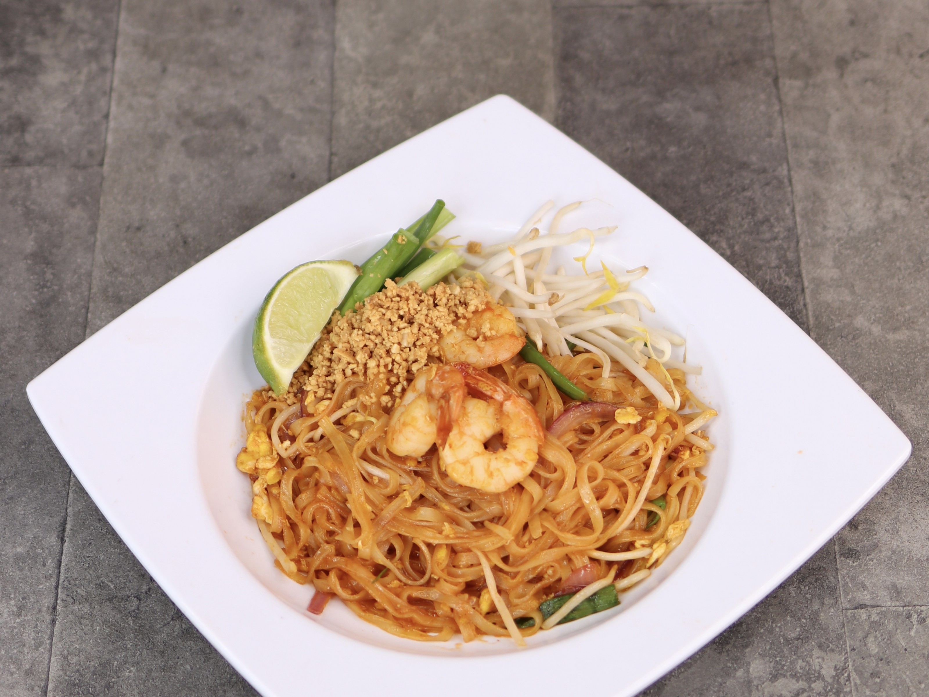 Pad Thai with prawns, lime and crushed peanuts on a white plate.